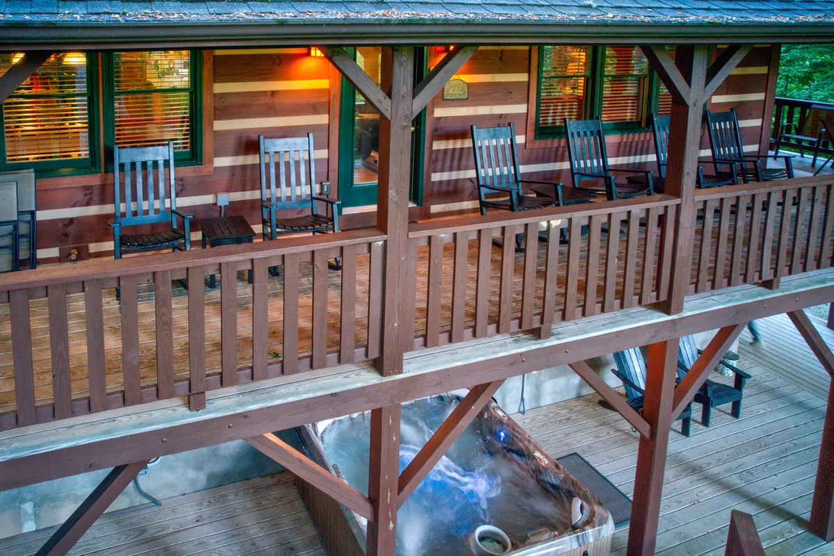 This image features a welcoming porch outfitted with classic wooden rocking chairs and a bubbling hot tub, framed by a rustic wooden railing. The porch overlooks the tranquil natural surroundings, offering an inviting space for relaxation and soaking in the mountain air. The combination of outdoor seating and hot tub creates a setting for both quiet mornings and social evenings.
