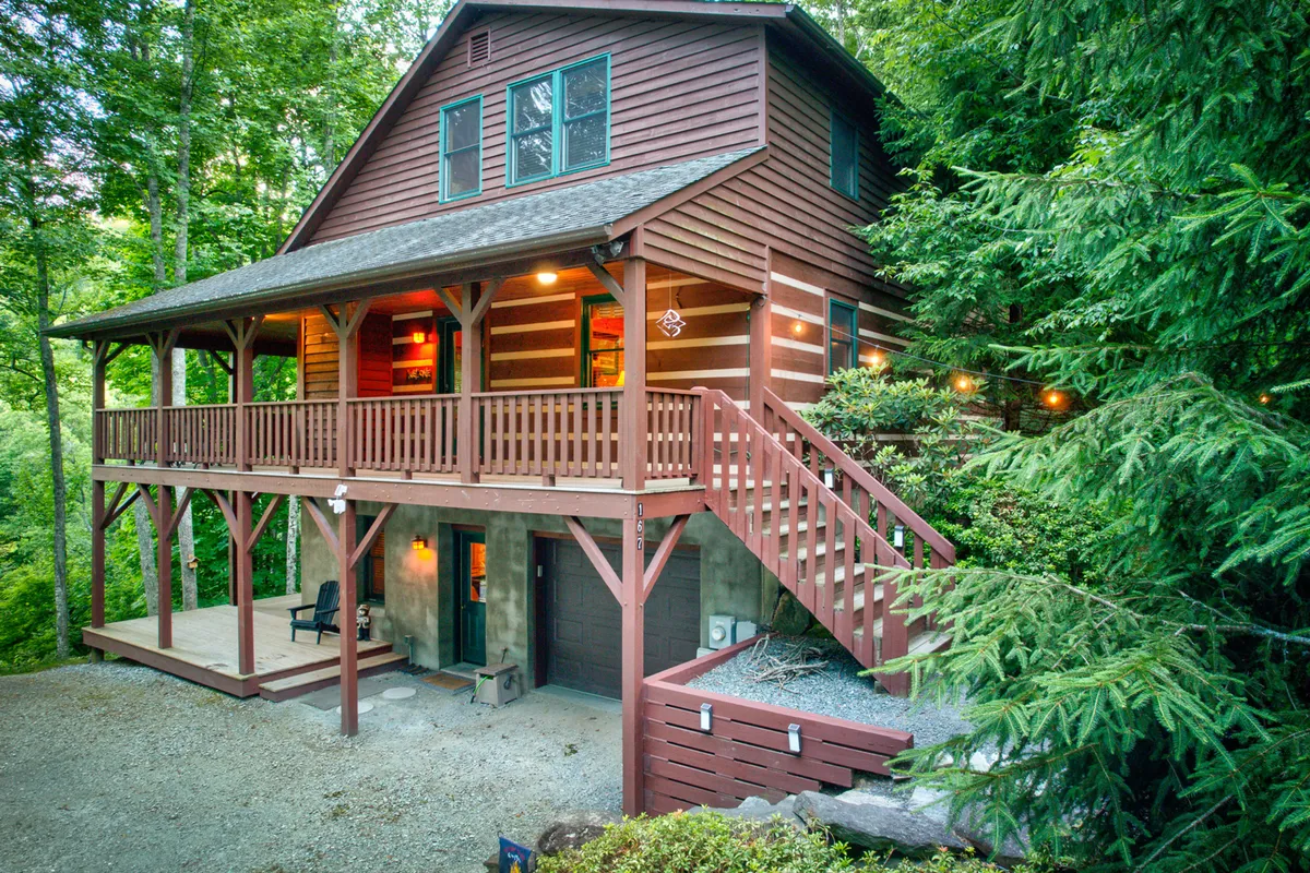 A spacious wooden deck bordered by railings, with large windows overlooking the surrounding lush greenery. The deck features a staircase leading down, creating a seamless transition between indoor comfort and the outdoors. The overall setting is inviting and ideal for socializing, relaxing, and enjoying natural views.