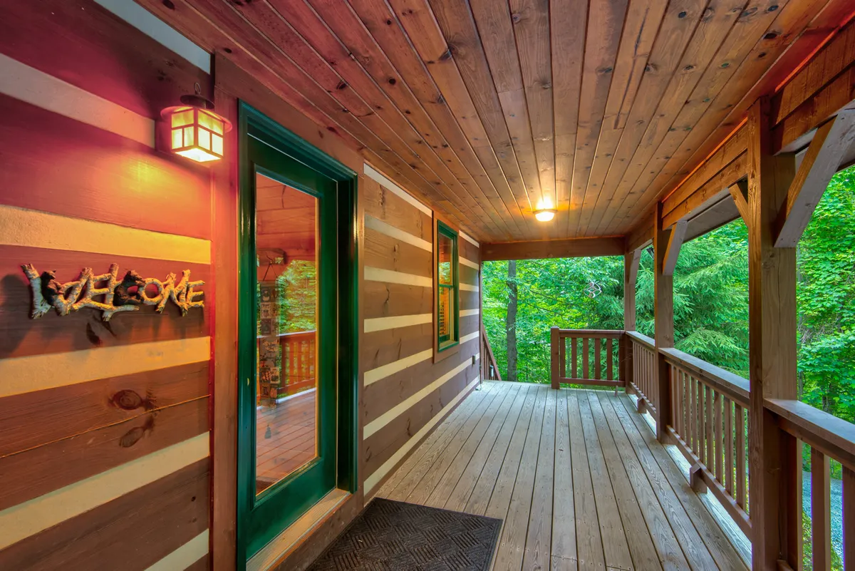 The welcoming front entrance features a charming green door, wooden beams, and lush surrounding greenery. The porch area invites guests to pause and take in the tranquil setting, with space for both people and pets to linger and enjoy the fresh air.