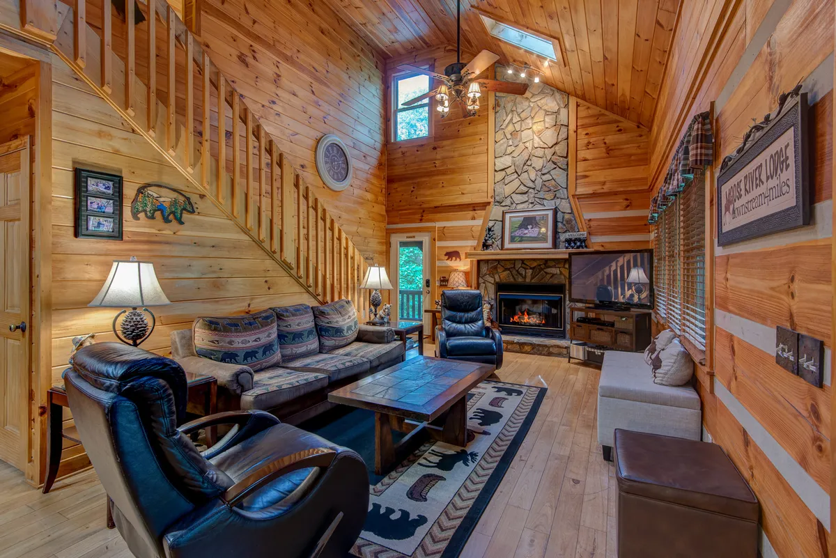 A stylish, inviting living room with a decorative fireplace, wooden staircase, plush sofa set, and tasteful wall art. The room is illuminated by natural light pouring in from large windows, setting the stage for movie nights and relaxed socializing.