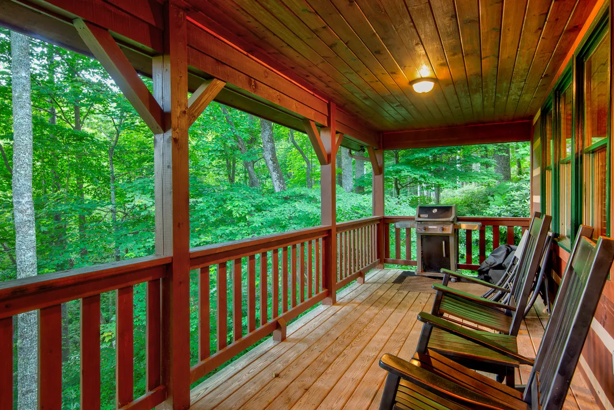 A tranquil porch furnished with classic rocking chairs and a grill, framed by wooden railings and lush greenery. The space invites guests to relax with morning coffee, enjoy evening barbecues, or simply take in the serene surroundings.