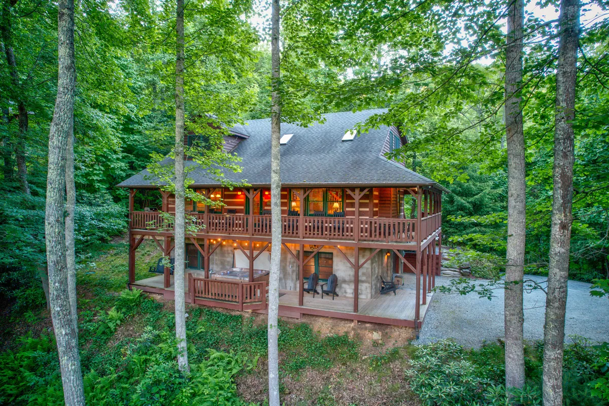 This image features a wooden balcony surrounded by tall trees, with comfortable patio chairs arranged to take in the lush, natural scenery. The large windows and open space suggest easy indoor-outdoor flow, perfect for relaxing and enjoying the mountain air. The abundance of greenery and the secluded setting evoke a tranquil, nature-connected atmosphere.