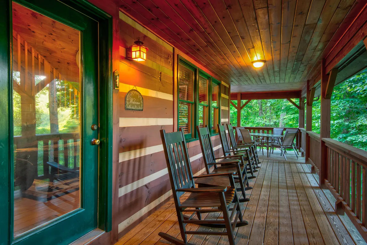 A close-up view of the porch featuring classic wooden rocking chairs positioned next to a sturdy wooden railing and a glass door leading inside. The scene radiates comfort and invites relaxation, with the natural beauty of the outdoors visible beyond the porch.