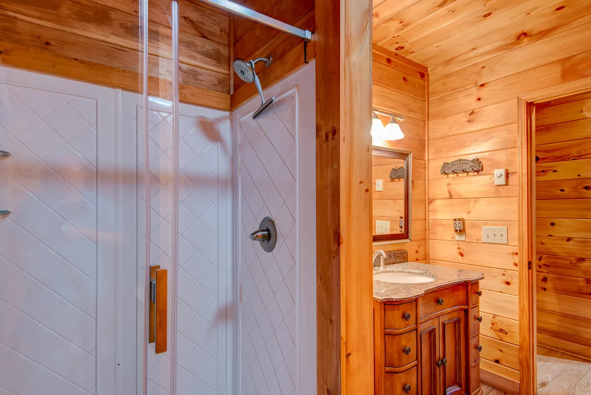 A well-appointed bathroom featuring a spacious shower area, vanity with sink, and rustic wooden walls. The mood is relaxing, perfect for unwinding routines.
